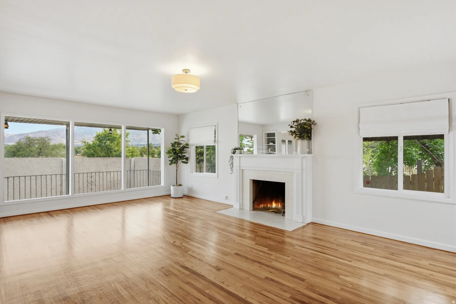 Hardwood flooring throughout, recessed fireplace with mantel, multiple large windows, and a semi-flush mount ceiling light fixture