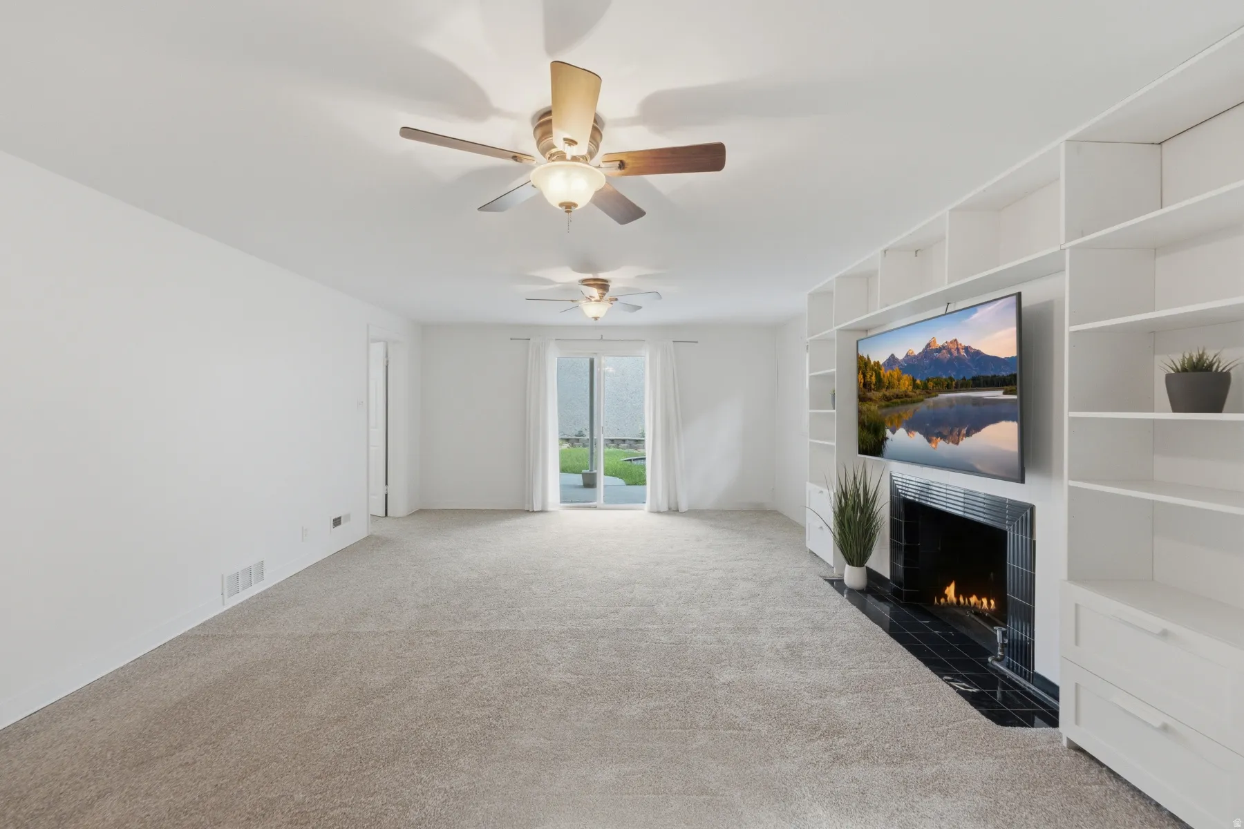Spacious room with plush carpet flooring, multiple ceiling fans, and a built-in media center with shelving