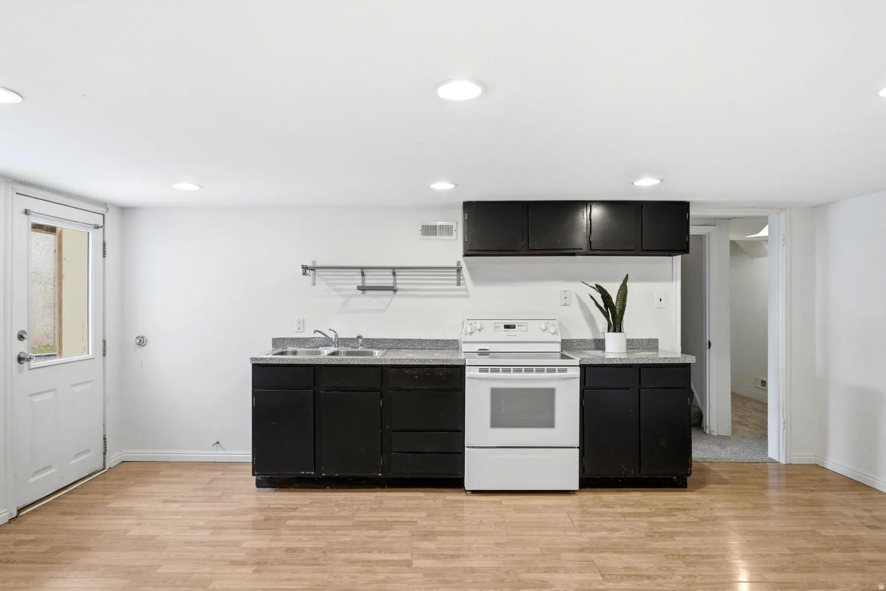 Compact kitchen area featuring wood-finish flooring, dark cabinetry, and a white electric range