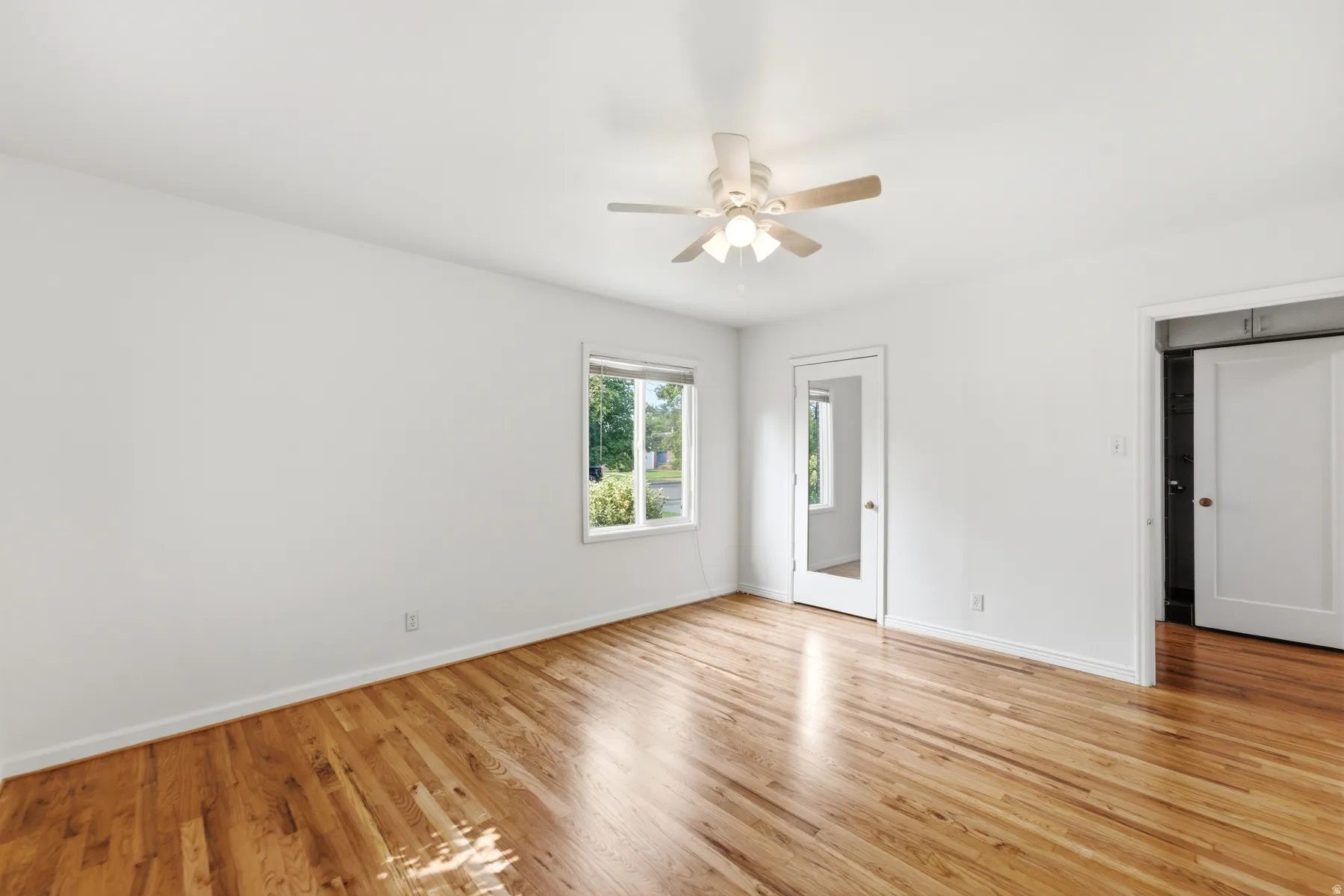 Hardwood flooring, white walls, ceiling fan with integrated lighting, glass-paneled door, and a multi-pane window