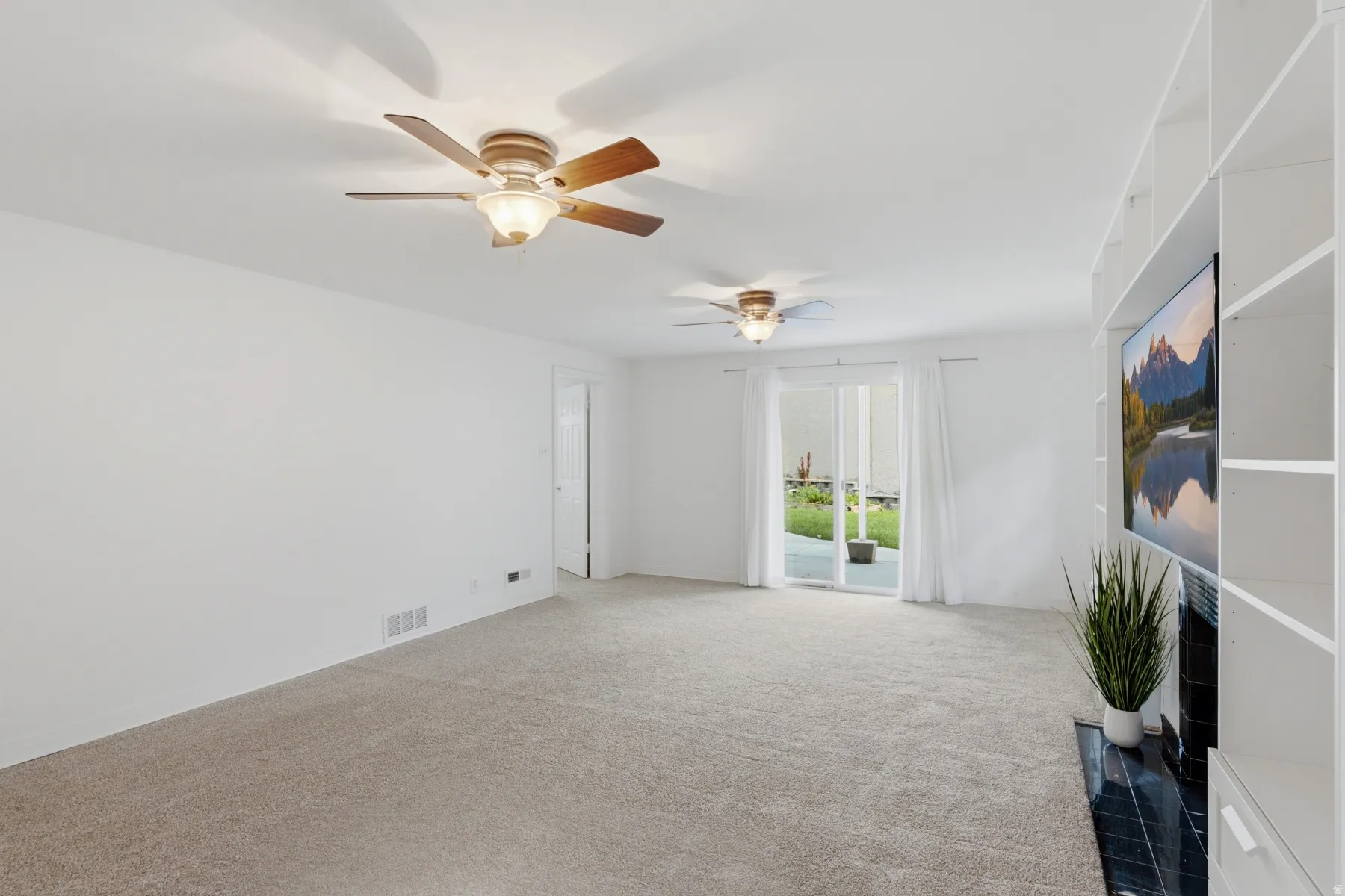 Expansive carpeted area featuring dual ceiling fans with lighting, built-in shelving, a fireplace with a dark tile surround, and a sliding glass door