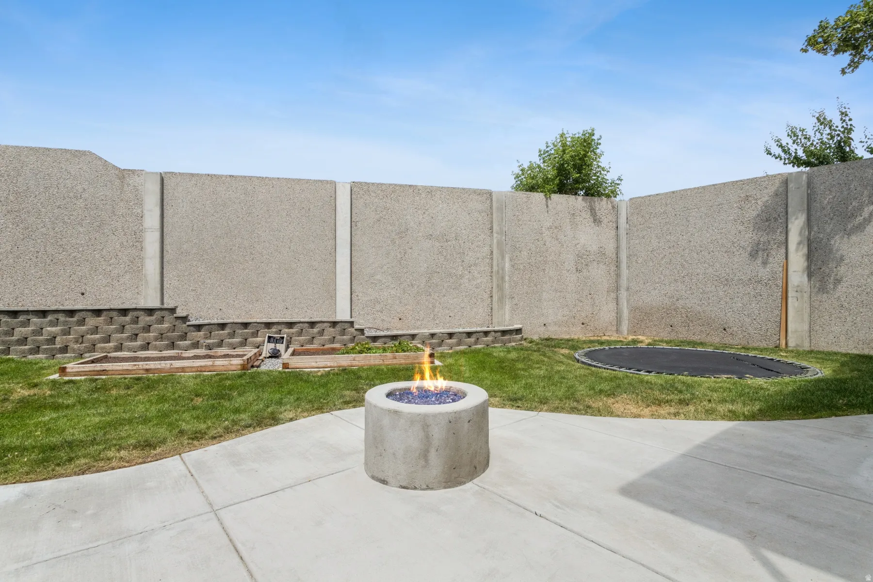 Concrete patio with a circular fire pit, expansive lawn, and concrete perimeter wall