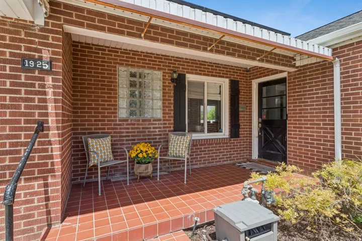 Brick exterior with a covered front porch, featuring a black entry door, a glass block window, and a window with black shutters