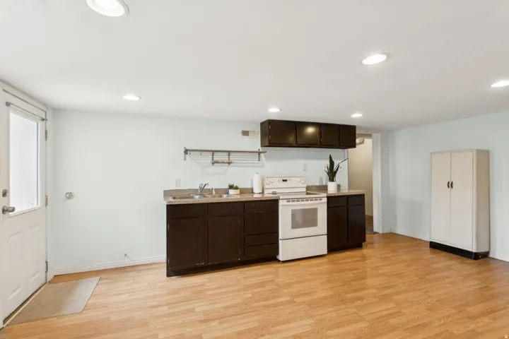 Kitchenette featuring dark wood cabinetry, a built-in electric range, and a stainless steel sink with a dark countertop