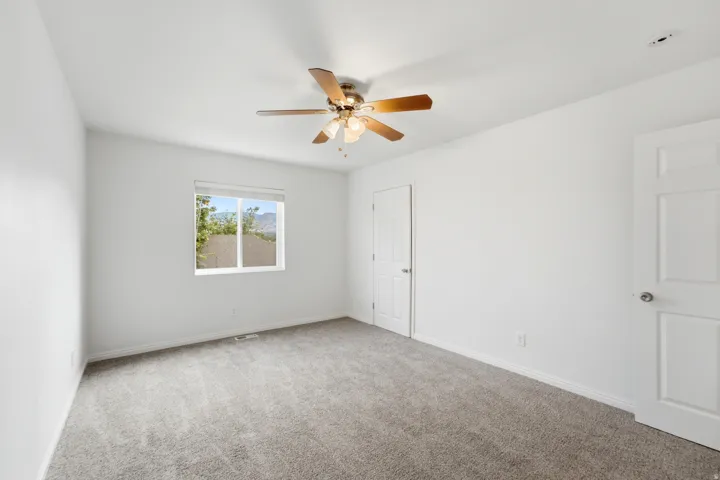 Neutral paint throughout with a ceiling fan, window, and grey carpet flooring