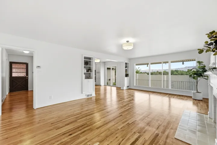 Hardwood flooring, built-in shelving, white fireplace surround, white tiled hearth, and large picture windows