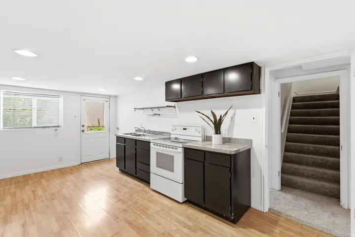 Compact kitchen with dark cabinetry, white appliances, and light-toned wood-finish flooring