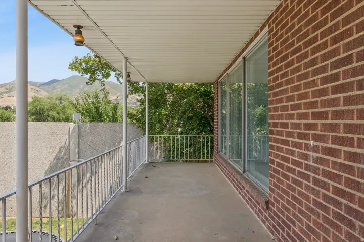 Covered balcony with concrete flooring, white metal railings, and a brick exterior wall