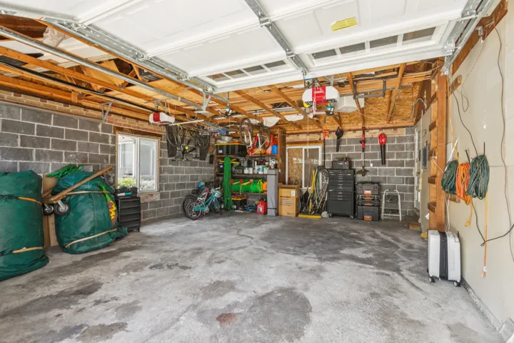 Spacious garage with exposed wood ceiling joists, durable concrete block walls, a concrete floor, and integrated window