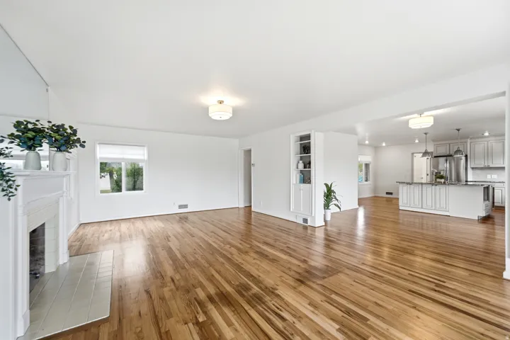 Hardwood flooring throughout, a white fireplace with a tile hearth, built-in shelving, and recessed lighting