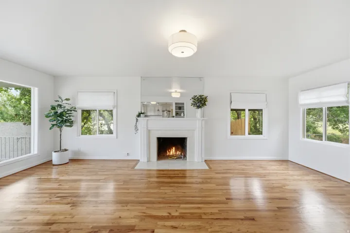 Hardwood flooring, white fireplace, multiple large windows, flush mount ceiling light fixture, crisp white wall paint