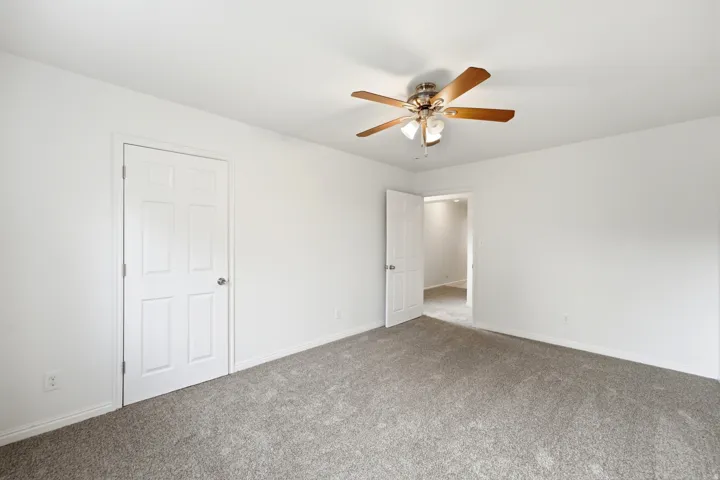 Neutral wall color, ceiling fan with light fixture, paneled doors, and gray carpet flooring