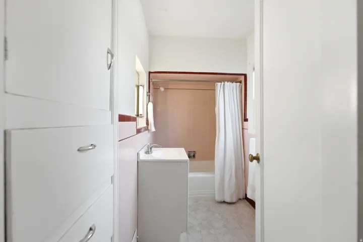 Built-in cabinetry with polished chrome hardware, a single vanity with an integrated sink, and a shower-over-tub combination