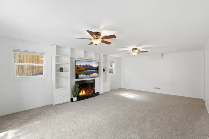 Built-in entertainment center with integrated shelving and drawers, fireplace with a black surround, dual ceiling fans, and neutral carpeting
