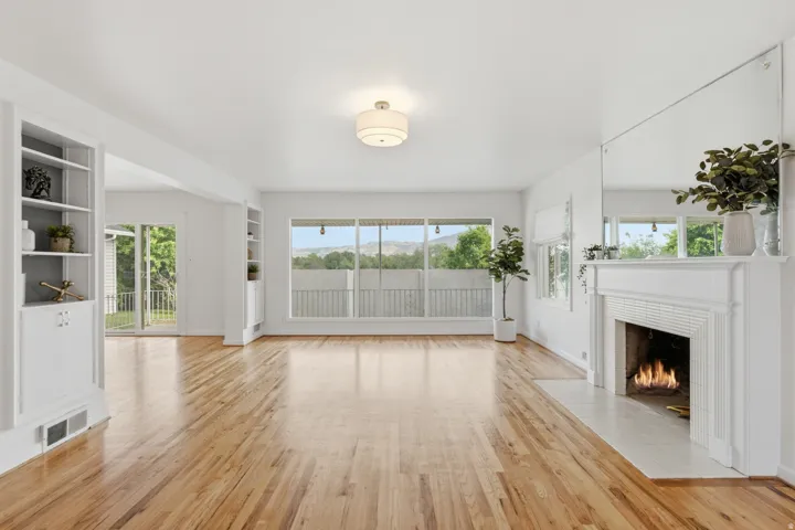 Hardwood flooring throughout, built-in shelving, white fireplace with tile hearth, large picture windows, and recessed lighting