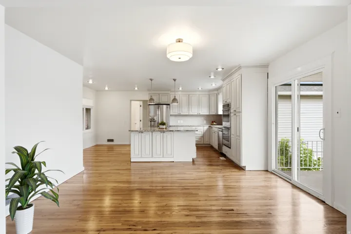 Hardwood flooring, kitchen island with granite countertop, white paneled cabinetry, stainless steel appliances, and sliding glass doors