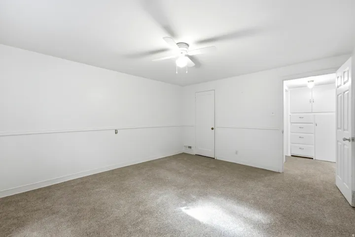 Recessed built-in storage, white paneled doors, wall-mounted ceiling fan, and carpeted flooring