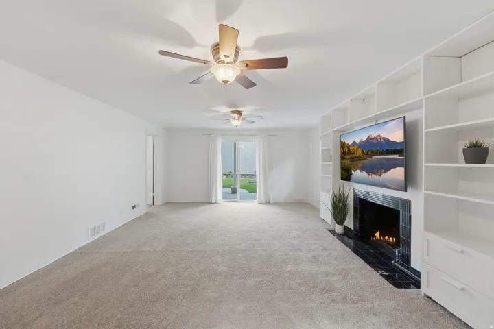 Spacious room with plush carpet flooring, multiple ceiling fans, and a built-in media center with shelving