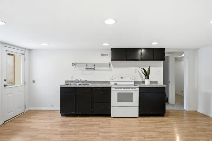 Compact kitchen area featuring wood-finish flooring, dark cabinetry, and a white electric range