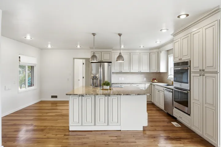Kitchen featuring light cabinetry, stainless steel appliances, a center island with a stone countertop, and wood-finish flooring