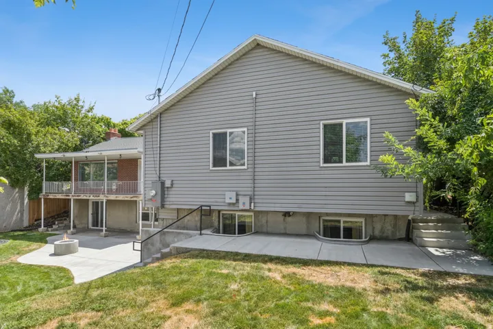Gray siding exterior with a covered balcony, lower-level patio with a built-in fire pit, multiple walk-out doors, and a concrete staircase