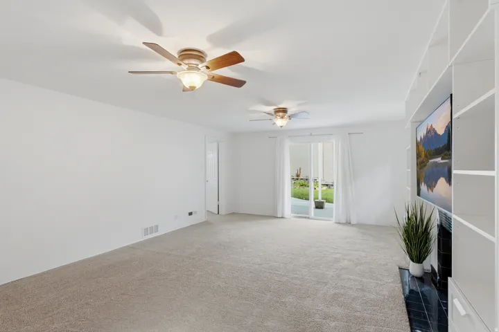 Expansive carpeted area featuring dual ceiling fans with lighting, built-in shelving, a fireplace with a dark tile surround, and a sliding glass door
