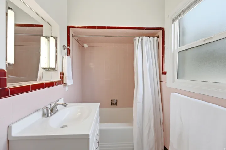 Vanity with integrated sink and brushed nickel faucet, tiled walls, built-in bathtub, and window with privacy glass