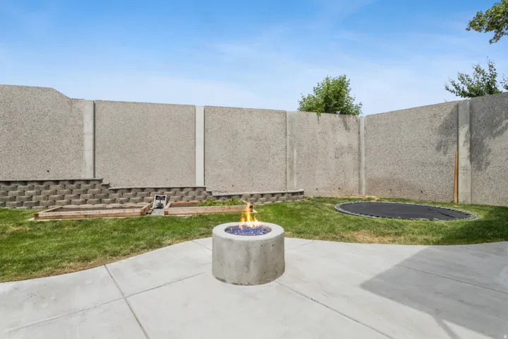 Concrete patio with a circular fire pit, expansive lawn, and concrete perimeter wall