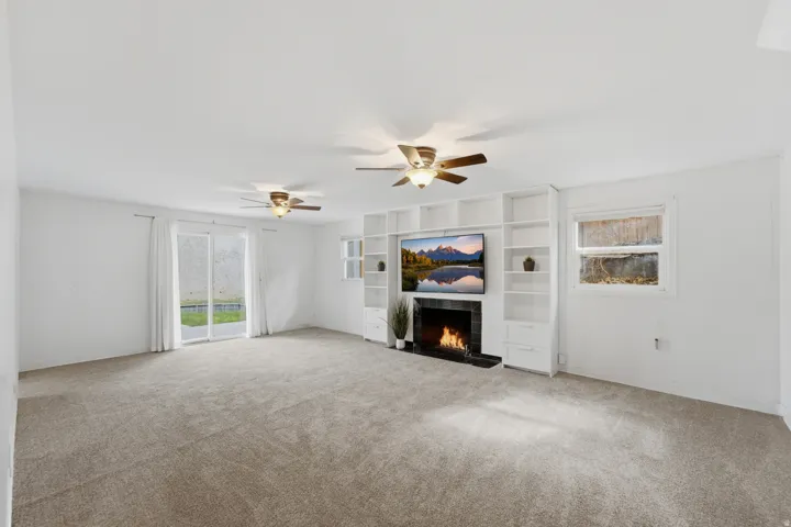 Spacious carpeted room featuring a built-in entertainment center, fireplace, recessed lighting, and sliding glass doors