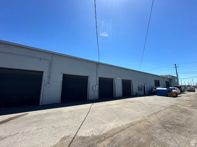 Commercial building featuring multiple roll-up doors, a flat roofline, and an asphalt parking area