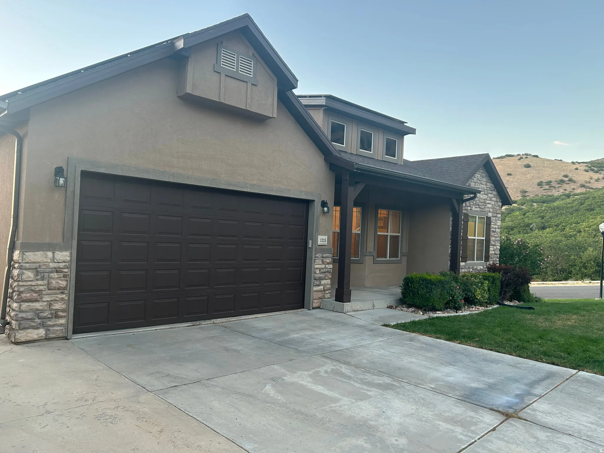 Stucco and stone exterior with a covered entry, dark paneled garage door, and a concrete driveway