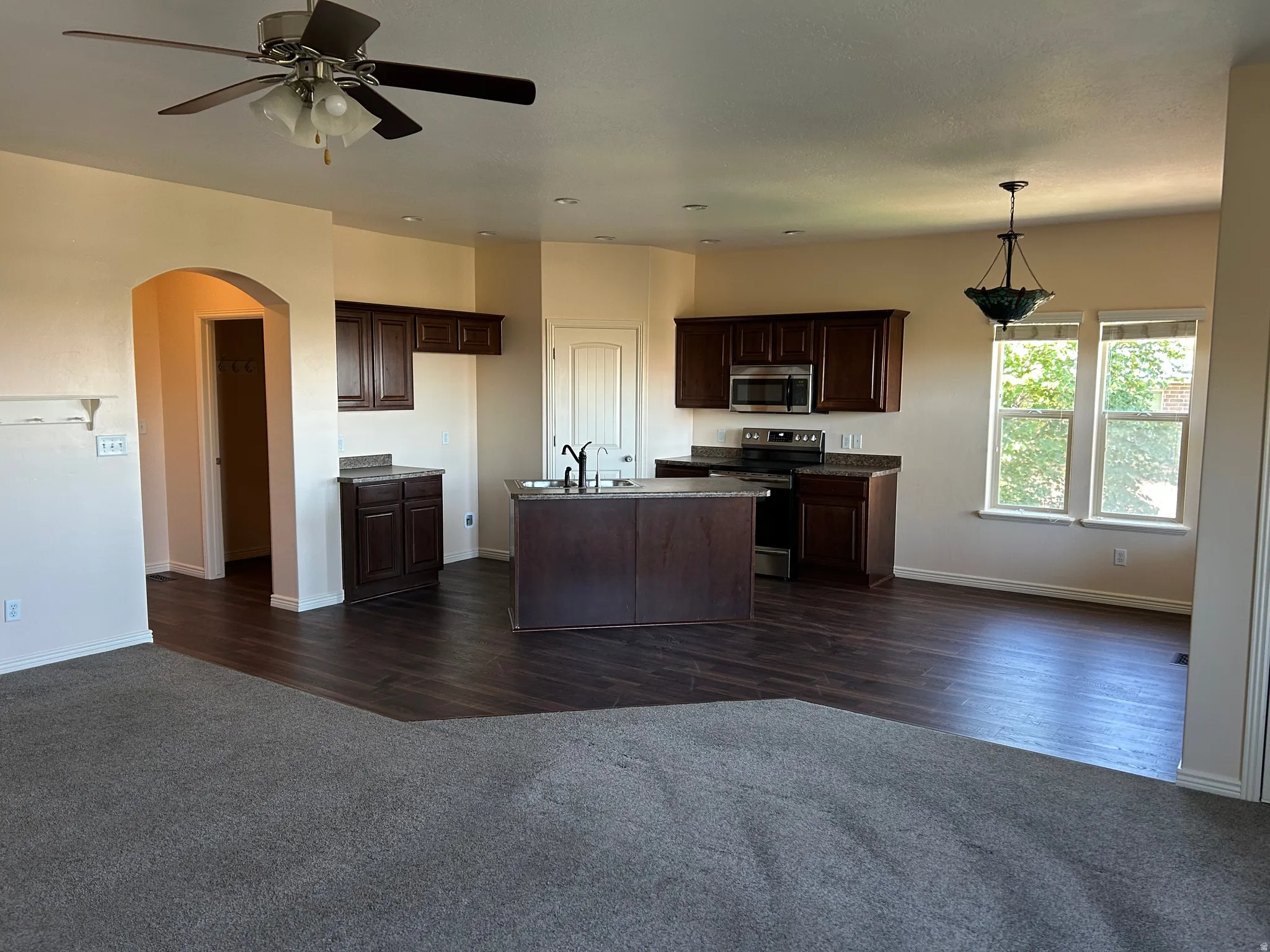 Open concept kitchen with dark wood-finish cabinetry, stainless steel appliances, and a central island with a sink