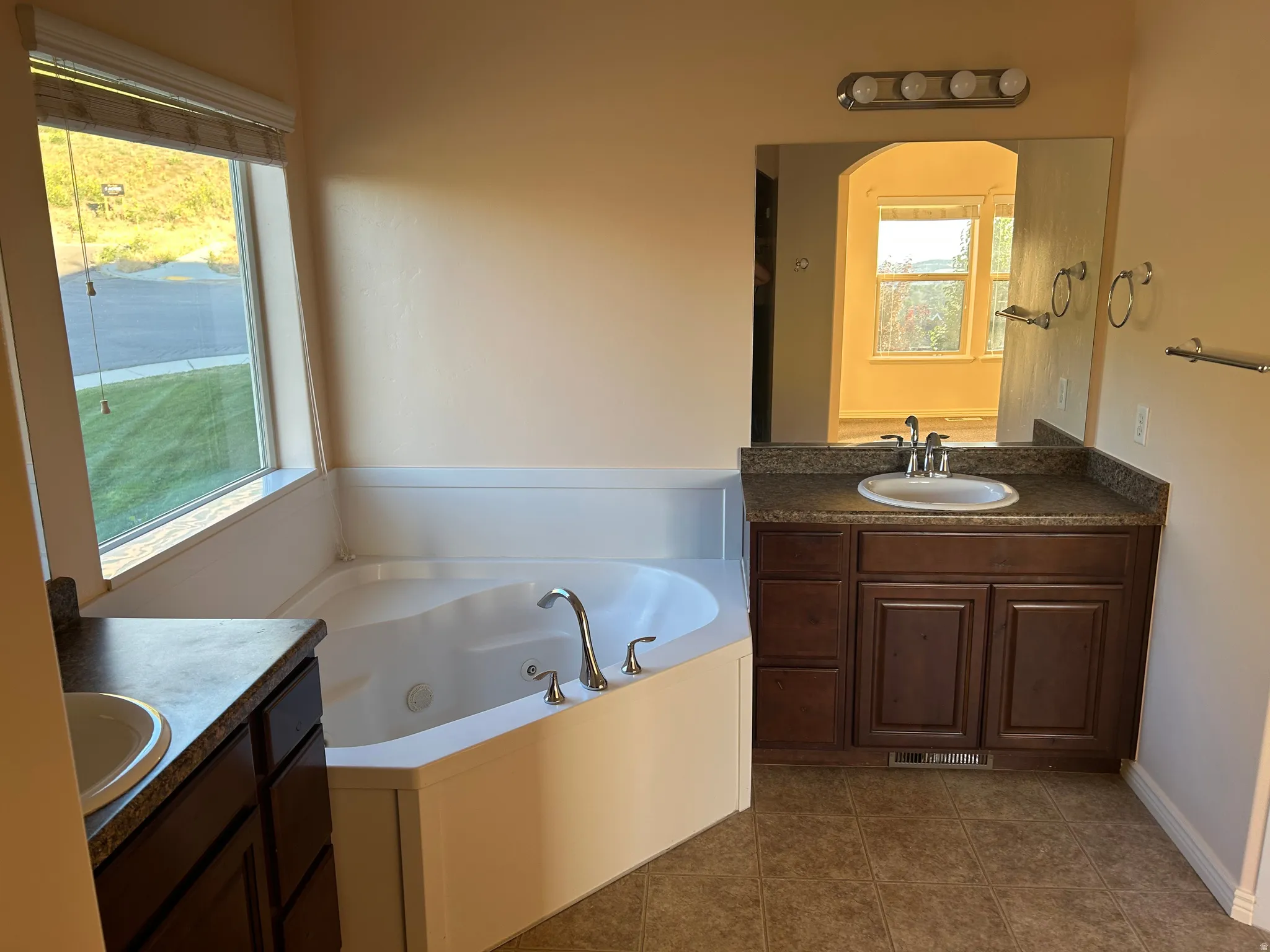 Soaking tub with corner placement, dual vanities with dark wood cabinetry, and a mirrored wall