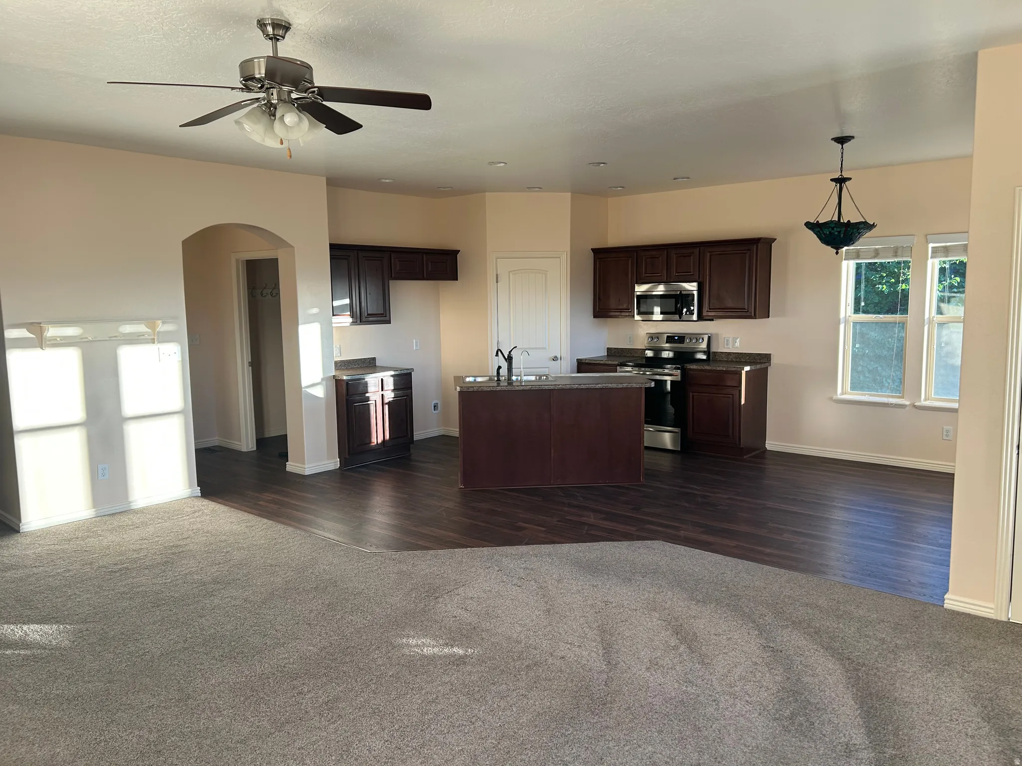 Open-concept living space with dark wood-finish flooring, dark wood cabinetry, stainless steel appliances, and a central island