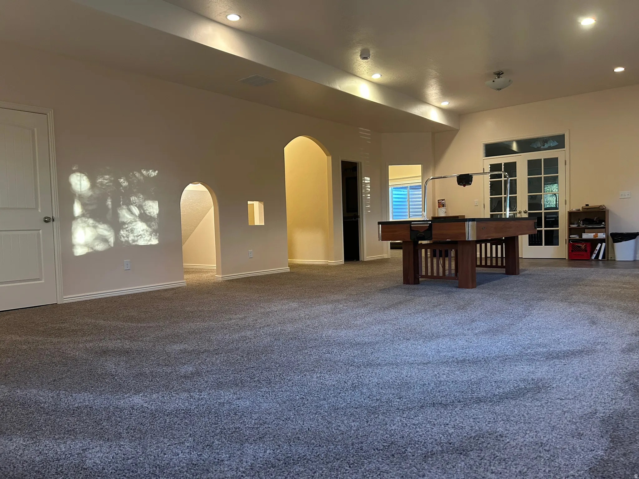 Spacious open-concept recreation room with recessed ceiling lighting, neutral carpet flooring, and architectural alcove features