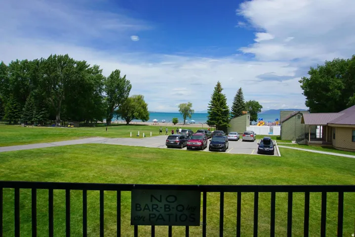 Expansive manicured lawn with mature tree-lined perimeter, multiple parking spaces, and direct water access
