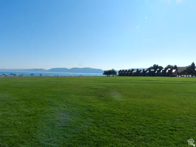Expansive green lawn bordering a body of water with distant mountains and a row of residential structures