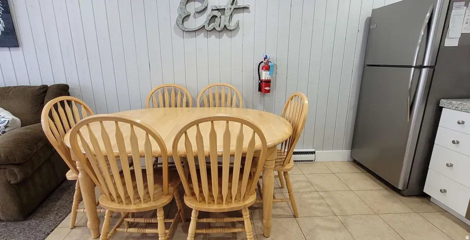 Spacious kitchen and dining area featuring a wood-finish dining table with seating for six, tile flooring, stainless steel refrigerator, and ample cabinet storage