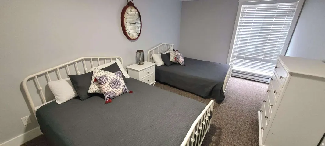 Carpeted room with light grey walls, a single window with blinds, and a white nightstand