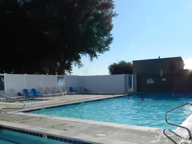 Swimming pool with surrounding concrete decking, white privacy fencing, and adjacent spa