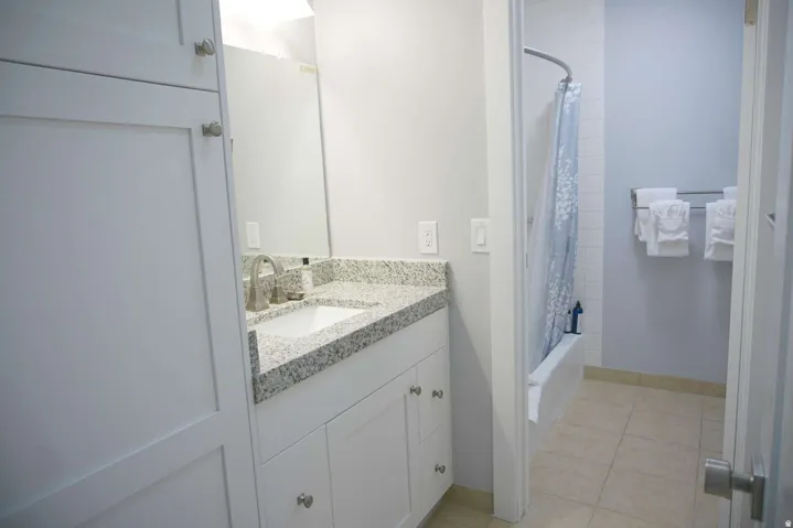 White shaker-style cabinetry, granite countertop, undermount sink with brushed nickel faucet, tiled flooring, and a shower-tub combination