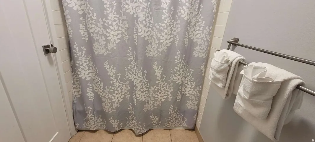 Tiled shower enclosure with a decorative shower curtain, complemented by a brushed nickel towel bar