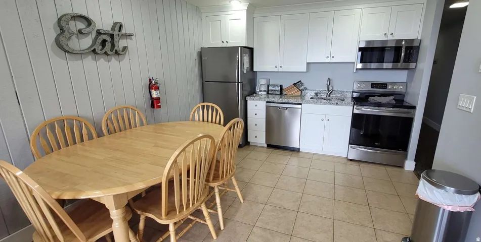 Kitchen featuring white cabinetry, stainless steel appliances, granite countertops, and tiled flooring