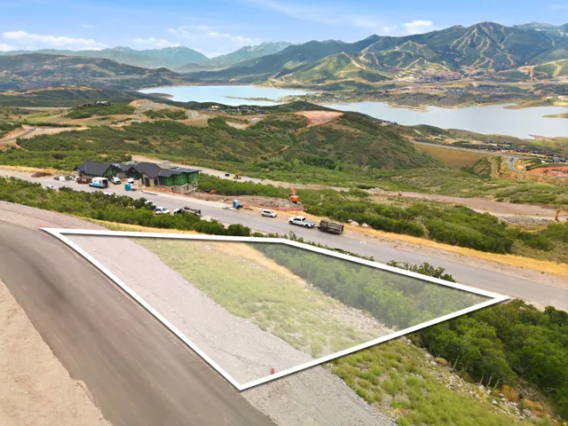 Expansive land parcel featuring partial green space and a paved road, set against a backdrop of distant mountains and a large body of water
