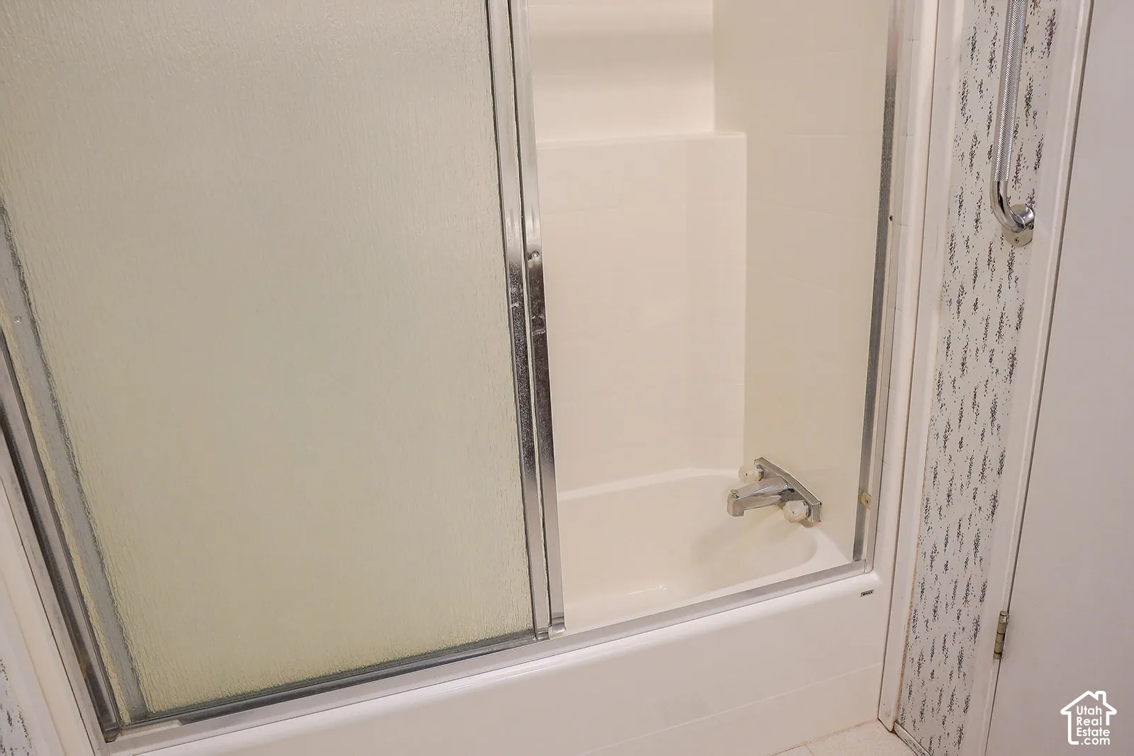 Tub and shower combination with sliding frosted glass doors, chrome hardware, and a grab bar