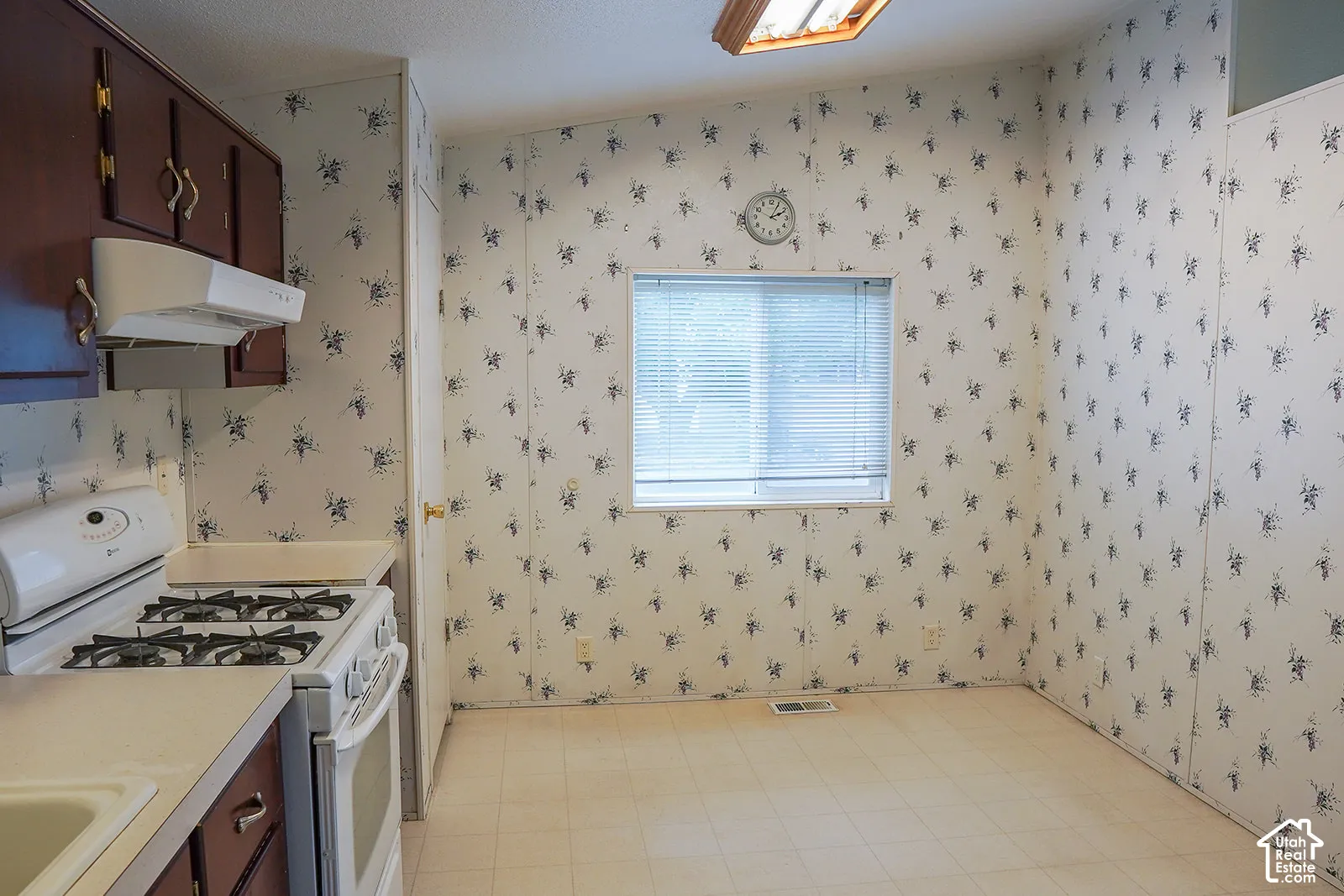 Brown wood-finish cabinetry, white countertop, white gas range, and a window with horizontal blinds