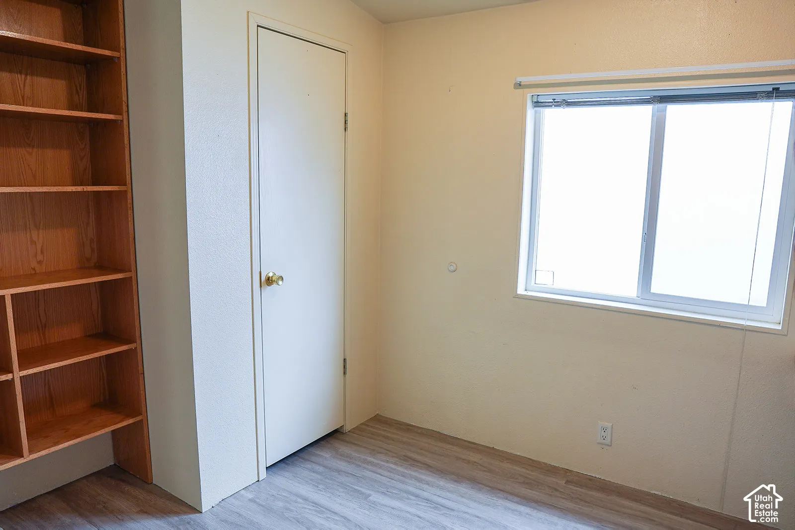 Wood-finish flooring, built-in wooden shelving, and a single window with a white frame