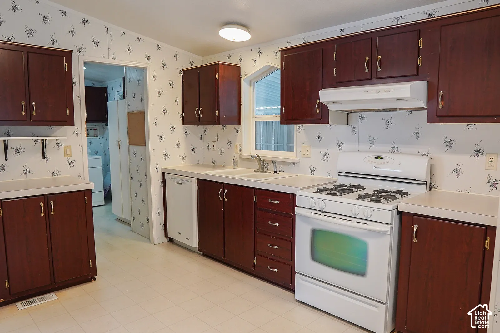 Kitchen featuring wood-finish cabinetry, white countertops, a white gas range, a white dishwasher, and a double basin sink