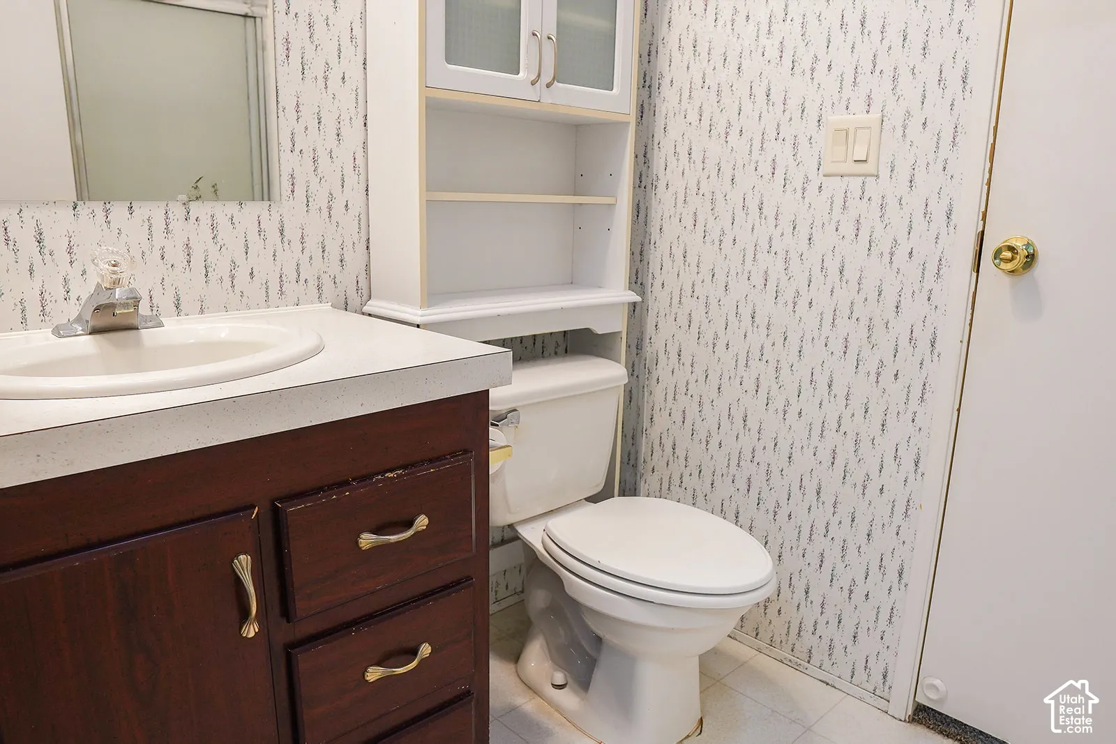Bathroom featuring a dark wood-finish vanity with an integrated sink, an overhead wall cabinet, and a white toilet