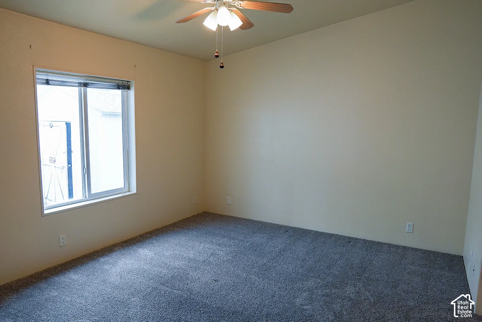 Neutral wall color, ceiling fan with light fixture, window with blinds, and grey carpet flooring
